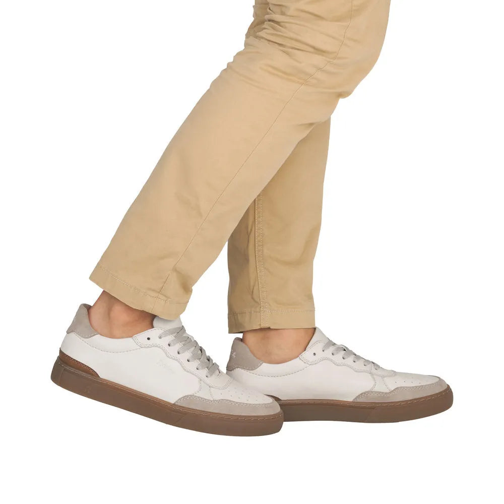 Men's white leather lace-up shoes with beige suede accents and brown soles, styled casually with beige pants.