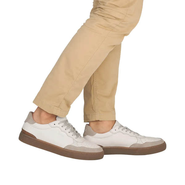 Men's white leather lace-up shoes with beige suede accents and brown soles, styled casually with beige pants.
