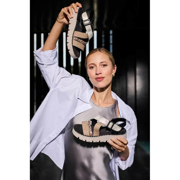 Woman holding and showcasing Rieker V1063-90 multi-touch fastening ladies' sandals with animal print and beige straps.