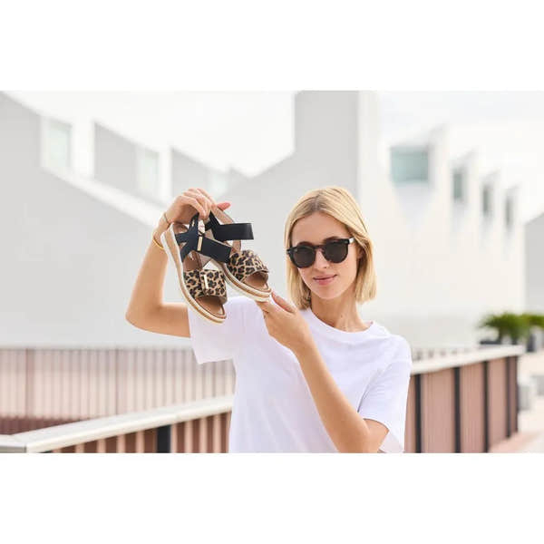 Woman holding Rieker V4181-00 women's wide fit multi-touch fastening leopard print sandals outdoors.