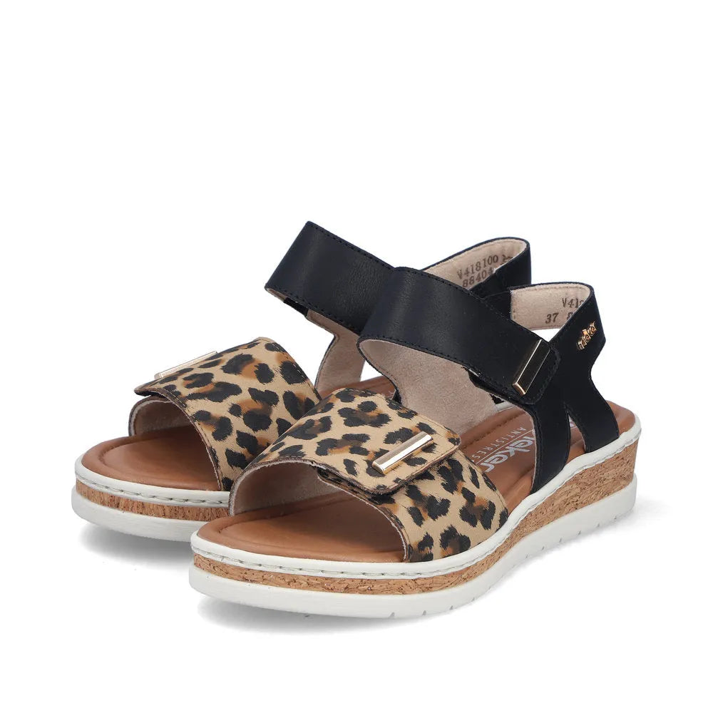 Rieker V4181-00 women's wide-fit sandals with leopard print front strap, black touch-fastening ankle straps, cork wedge heel, and white sole.