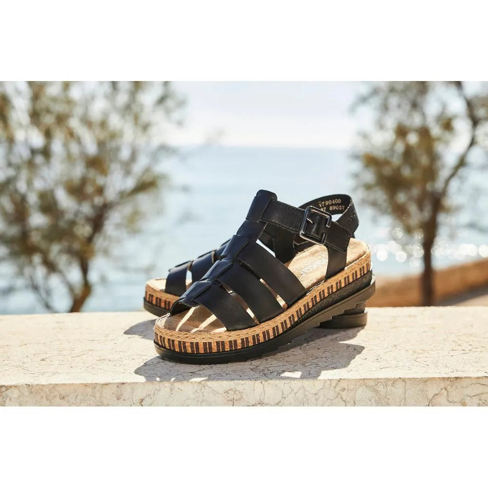 Rieker V7904-00 women's black leather touch-fastening sandals with a cork-style sole, outdoor setting, by the water.