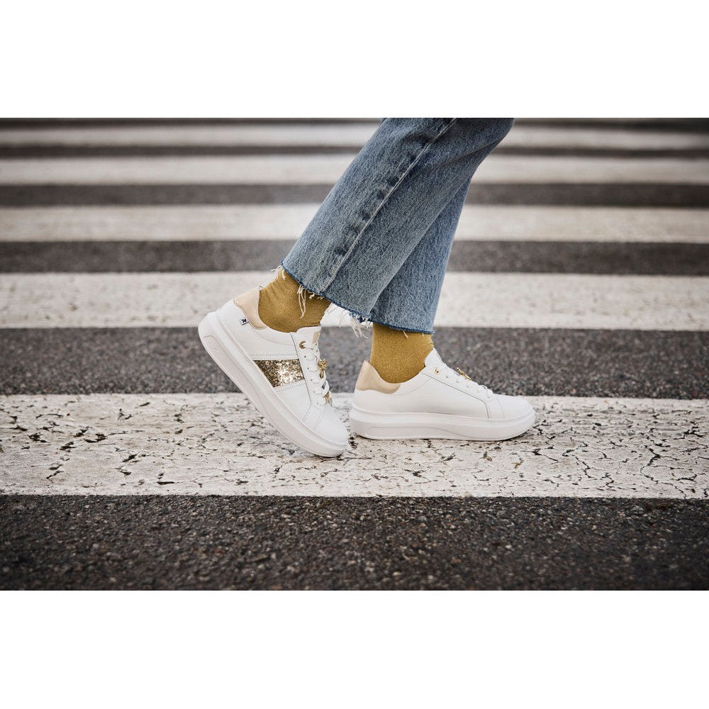 Rieker W1202-82 women's white and metallic leather lace-up trainers with gold accents, casual sneaker style, on a street crosswalk.