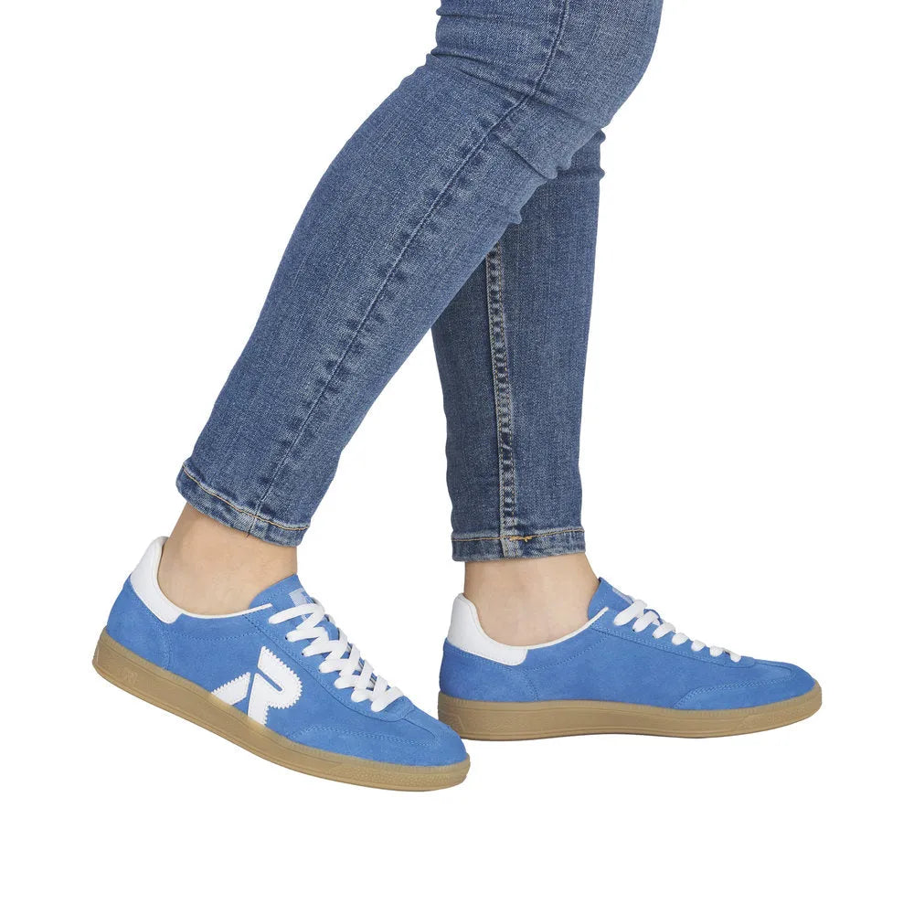 Light blue suede lace-up trainers with white accents and tan soles, worn with blue jeans.