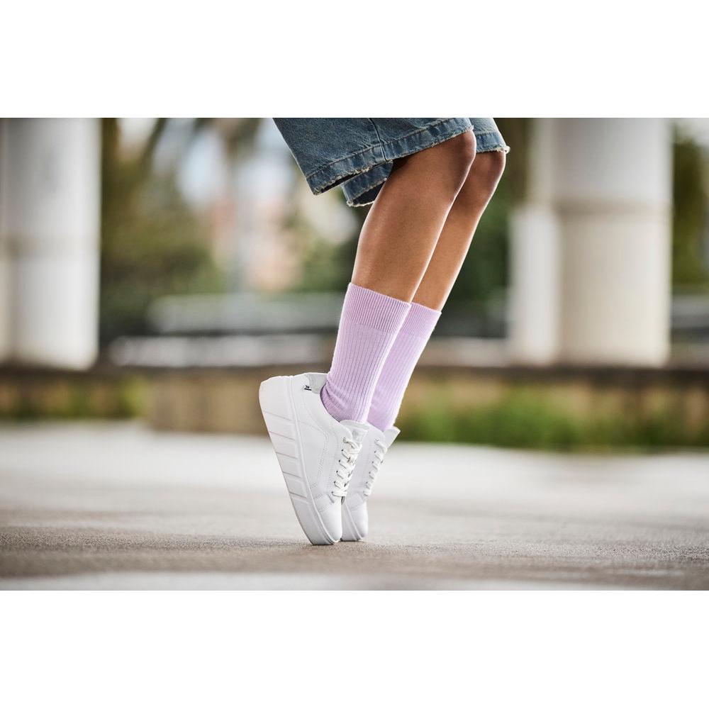 Rieker W2601-80 ladies white leather lace-up trainers with chunky sole, paired with pink socks, outdoor urban setting.