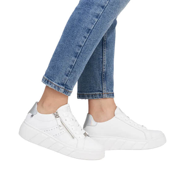 Rieker W2605-80 women's white leather sneakers with zip and laces, chunky sole, and iridescent accents, paired with blue jeans.