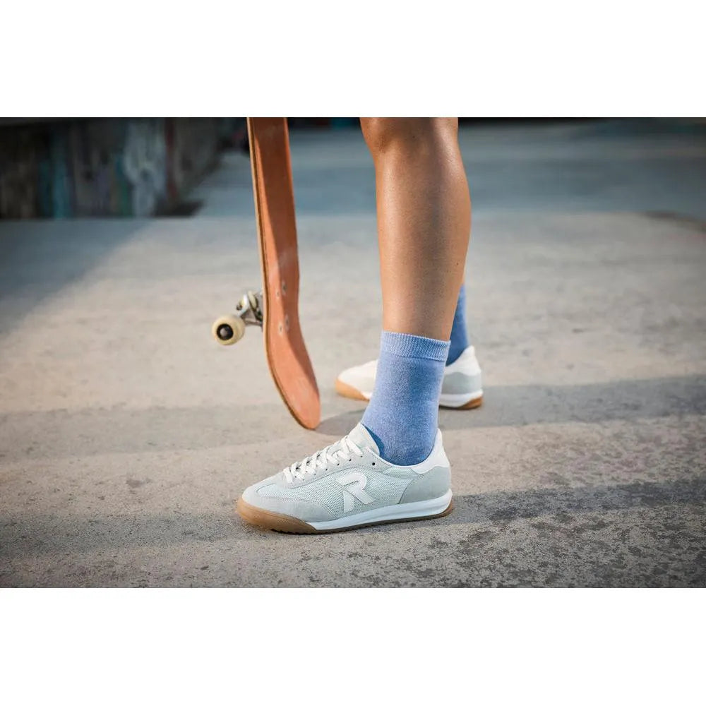 White sporty trainers with mint suede and textile upper, lace-up design, and gum rubber sole on a concrete surface.