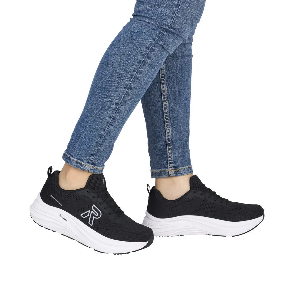 Black textile lace-up trainers with white cushioned midsoles and black outsoles, worn with blue jeans.