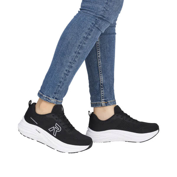 Black textile lace-up trainers with white cushioned midsoles and black outsoles, worn with blue jeans.
