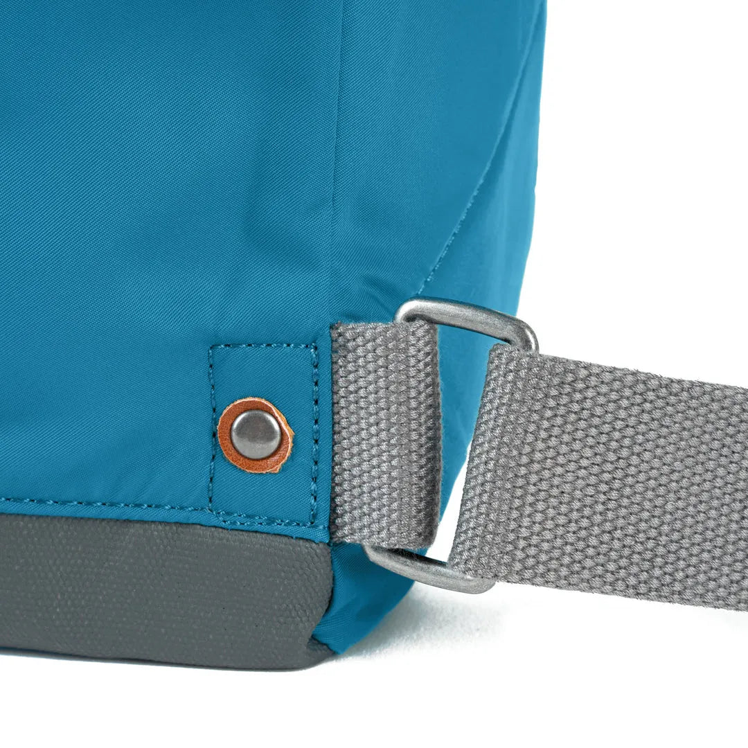 Close-up of Roka Bantry B Marine recycled nylon backpack strap and fabric, featuring durable grey strap, metal hook, and vibrant blue material.