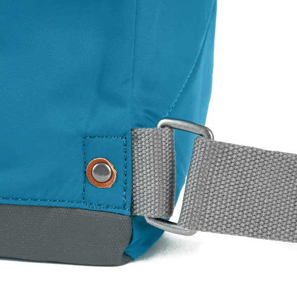 Close-up of Roka Bantry B Marine recycled nylon backpack strap and fabric, featuring durable grey strap, metal hook, and vibrant blue material.