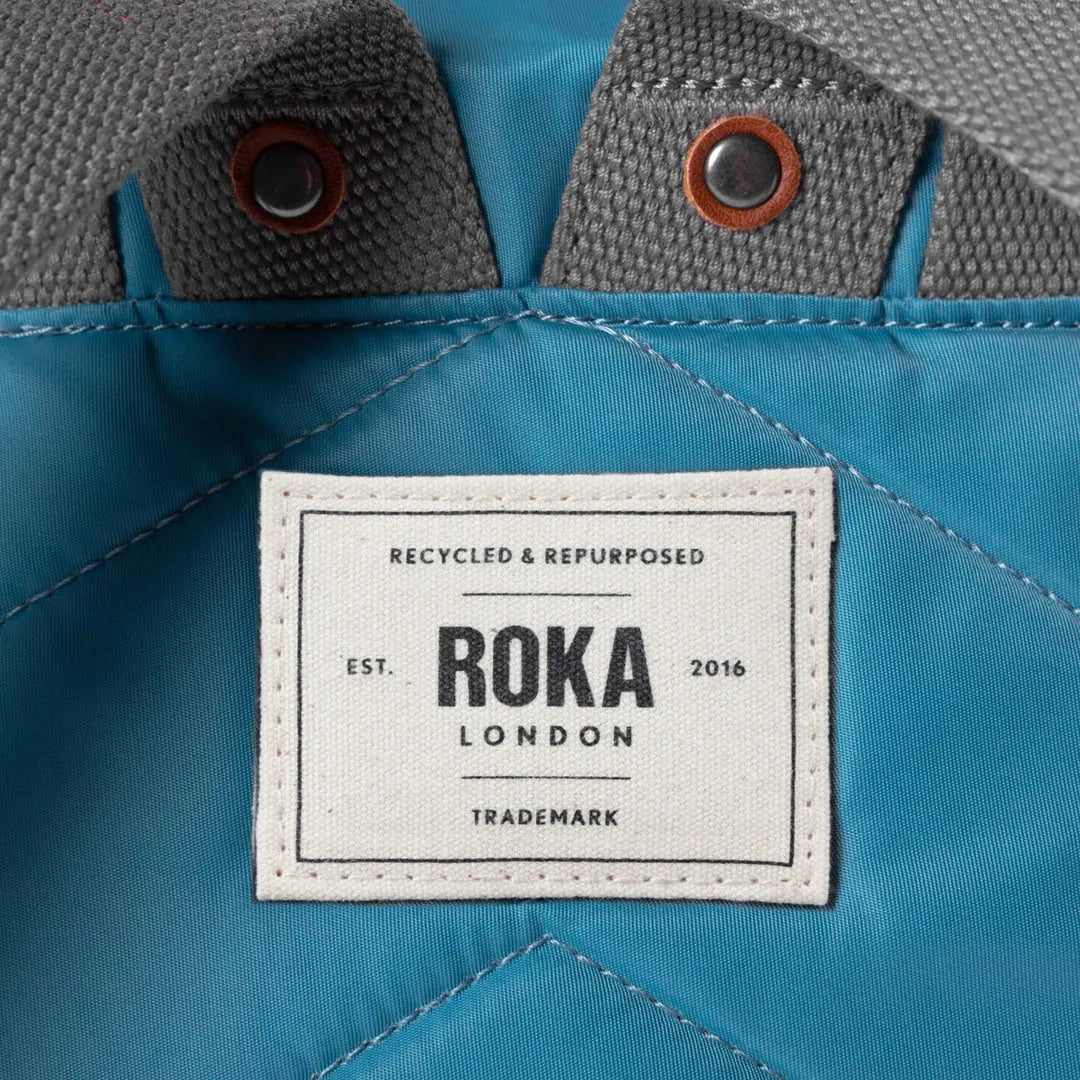 Roka London recycled nylon petrol backpack with grey fabric accents and leather-trimmed snap buttons.