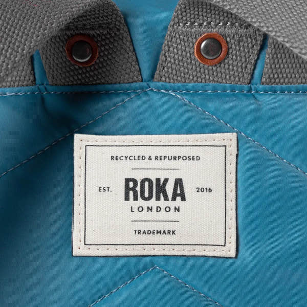 Roka London recycled nylon petrol backpack with grey fabric accents and leather-trimmed snap buttons.