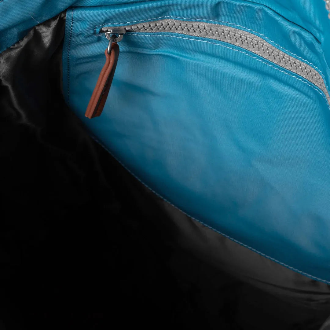 Roka Bantry B backpack made from recycled nylon, featuring a blue fabric with a zippered pocket and brown zipper pull.