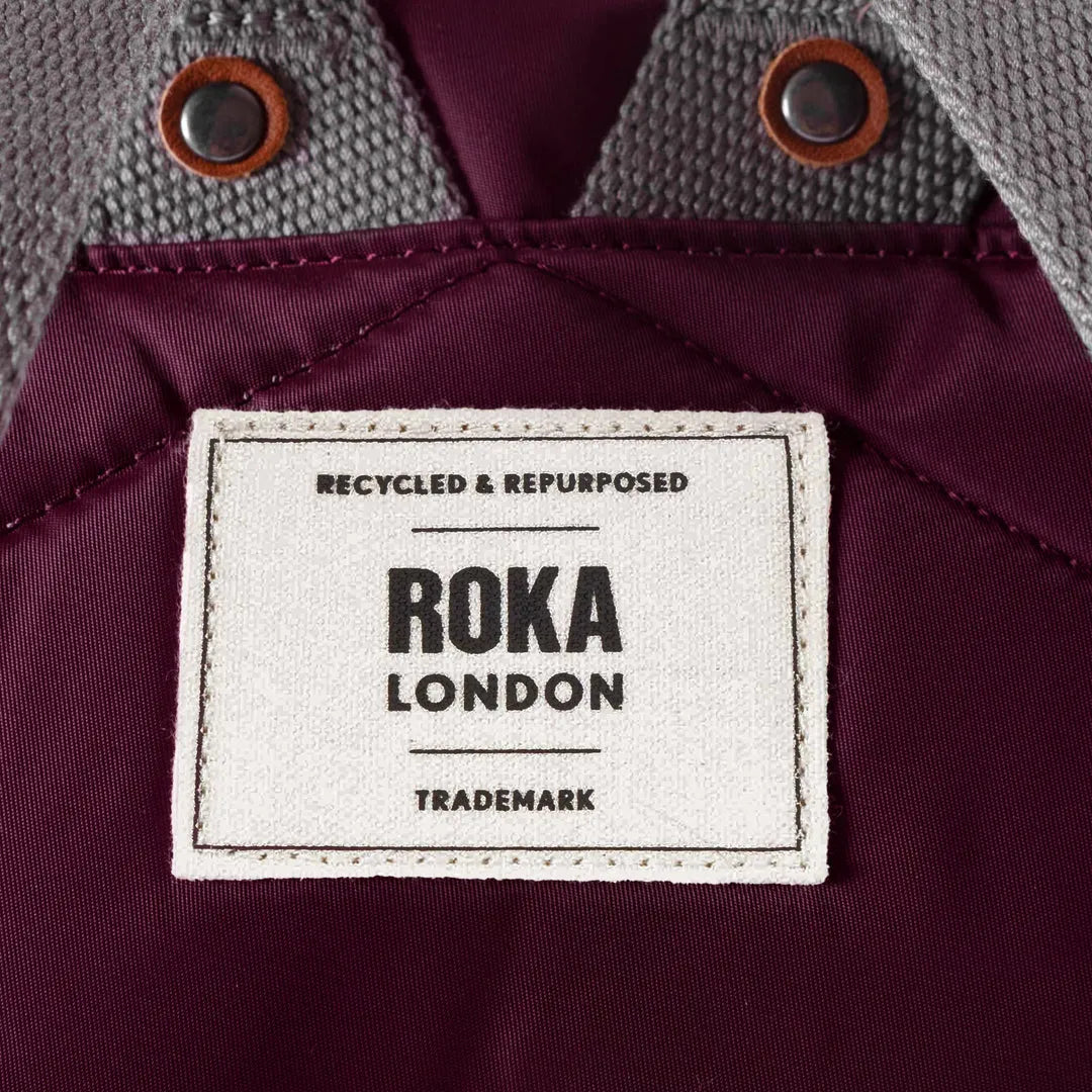 Roka Bantry B Plum Recycled Nylon jacket with label, burgundy interior, gray textured shoulder, and button details.