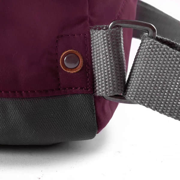 Roka Bantry B Plum recycled nylon bag strap with metal buckle and eyelet detail on burgundy fabric.