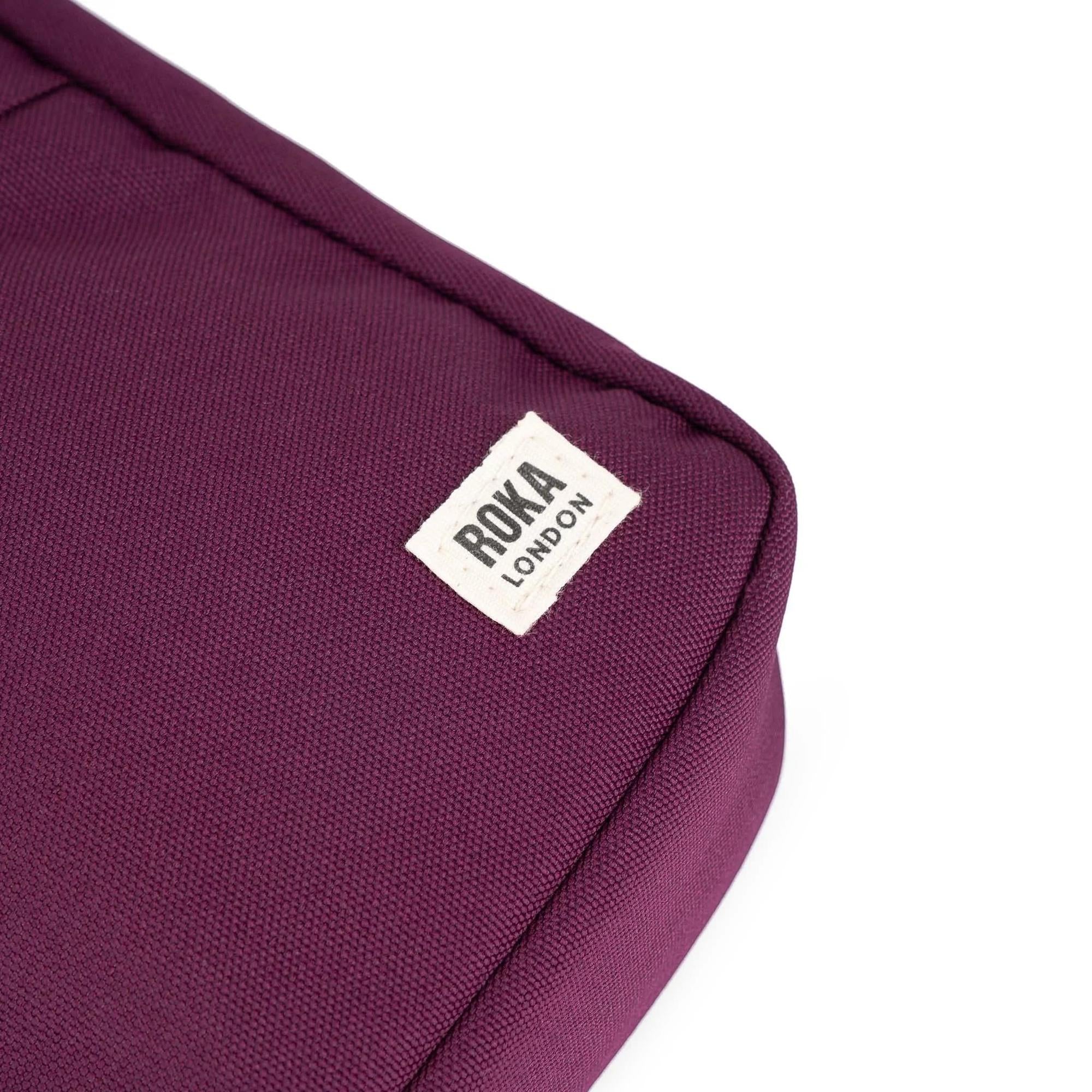 Roka Bond Cherry Lacquer recycled canvas bag, one size, with white Roka London label, in deep cherry color, close-up of corner and fabric texture.