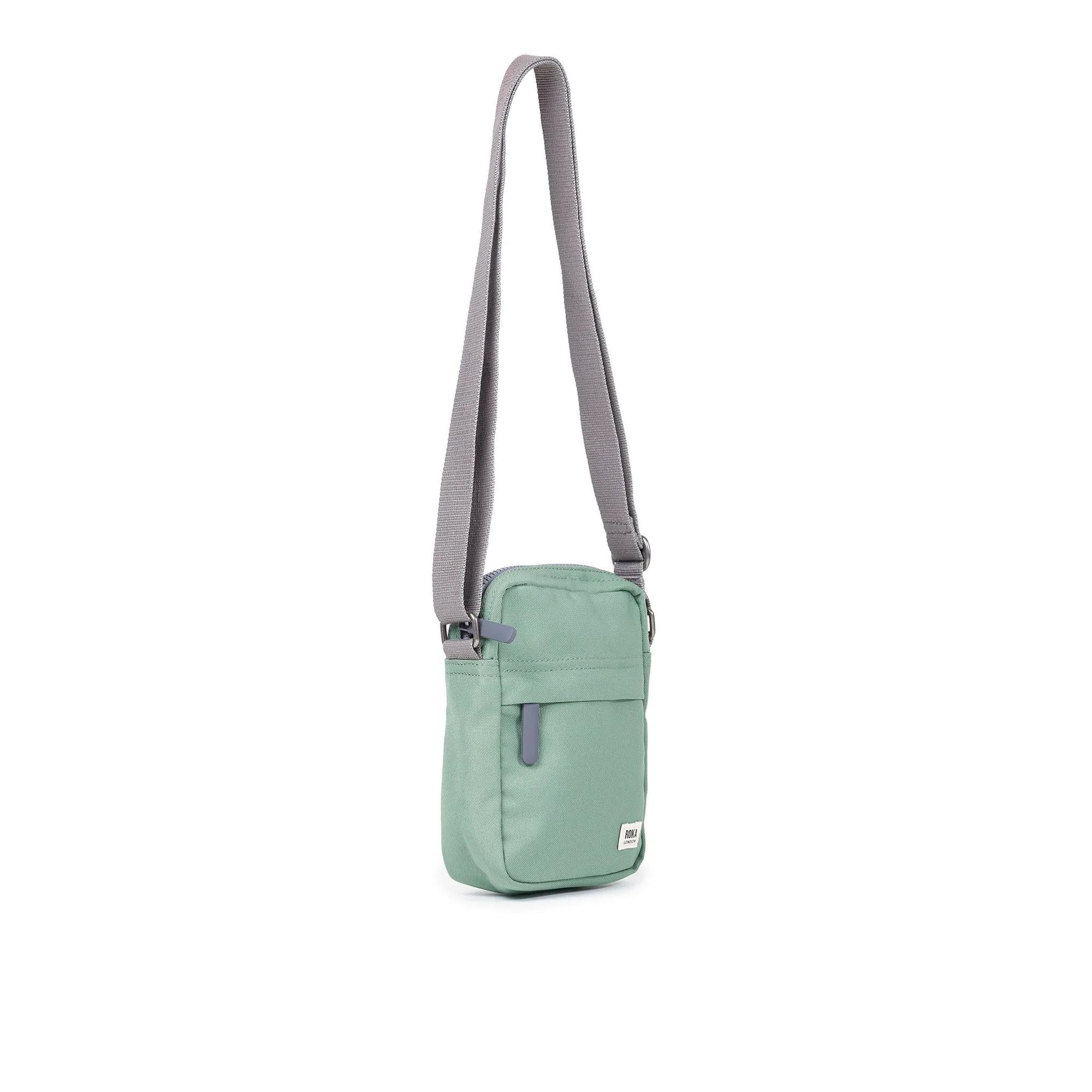 Roka Bond Frost recycled canvas crossbody bag with adjustable strap, mint green color, front pocket, and modern design.