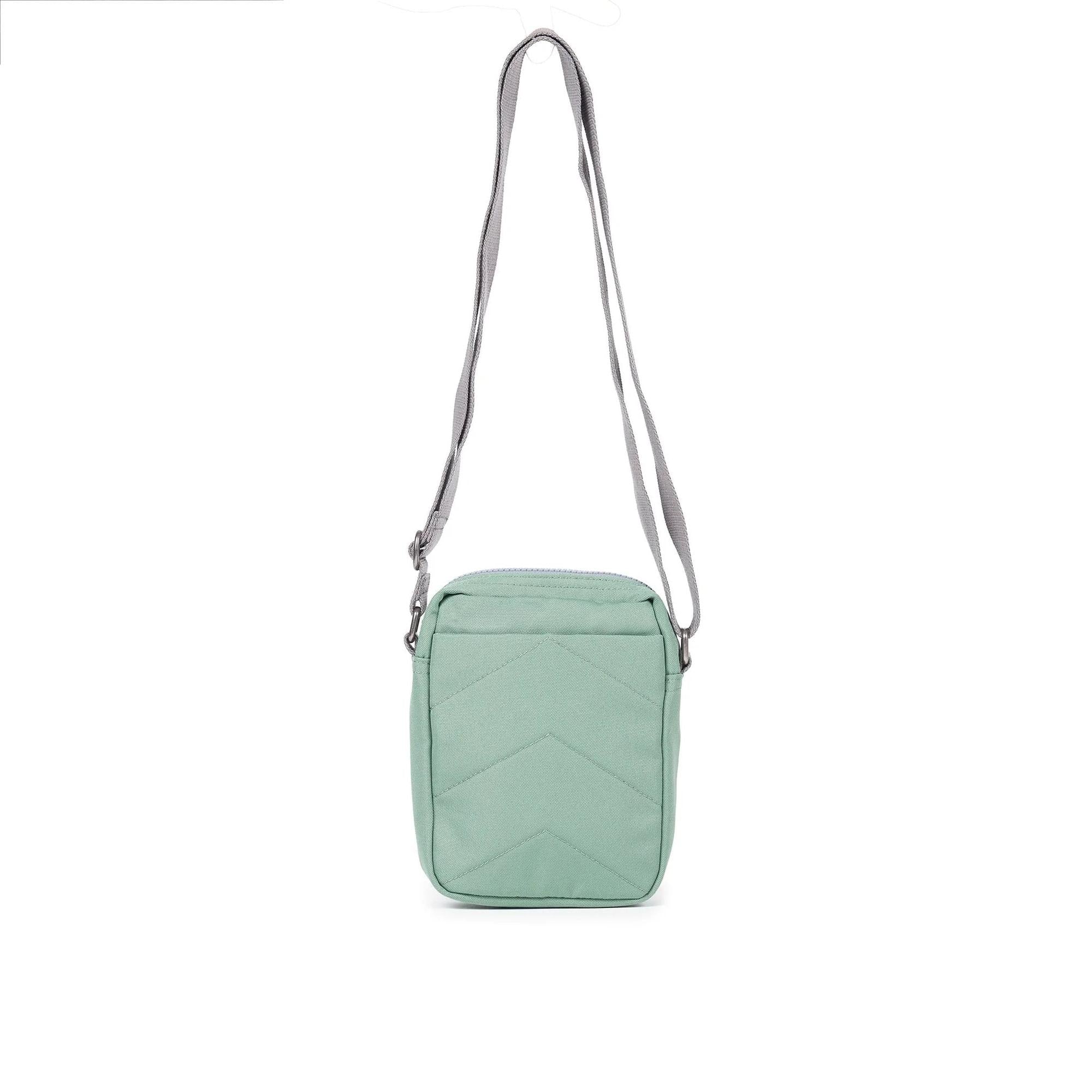 Roka Bond Frost recycled canvas crossbody bag, one size, light green with four chevron-stitched panels and adjustable gray strap.