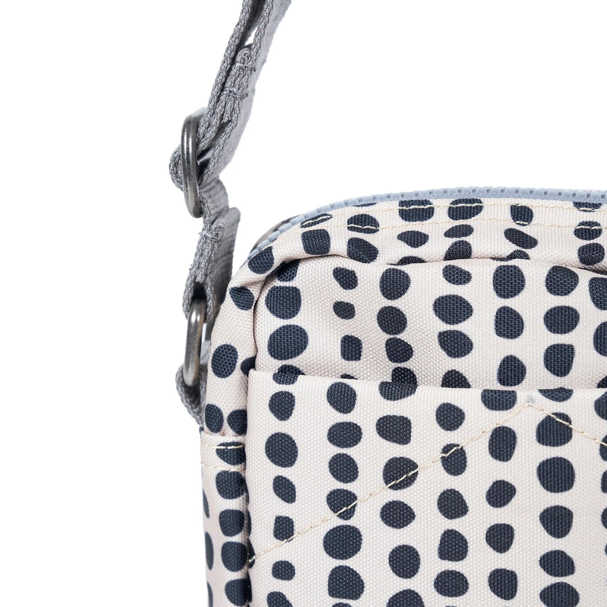 Close-up of Roka Bond linear dot recycled canvas bag with adjustable strap, navy polka dot pattern, and metal hardware.