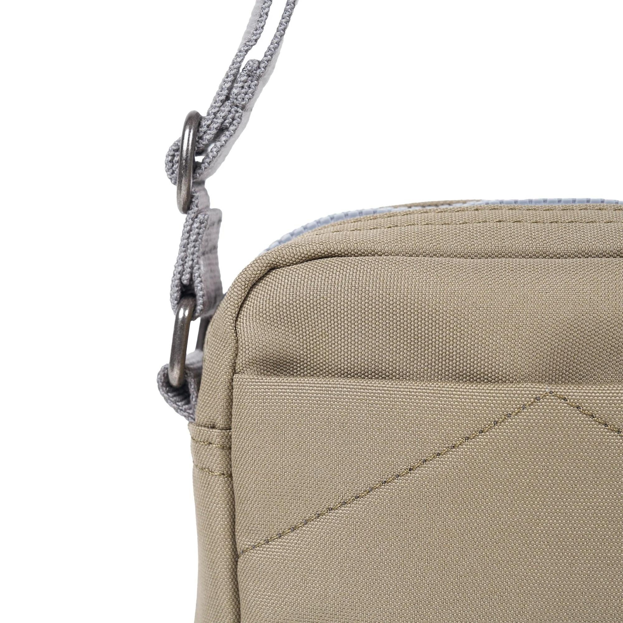 Roka Bond Taupe recycled canvas crossbody bag with adjustable gray strap, one size, close-up of top corner and stitching.