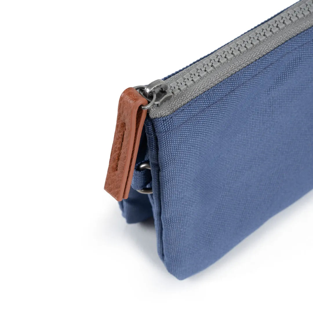 Roka Carnaby Burnt Blue Recycled Canvas bag with silver zipper and brown leather pull tab. High-quality eco-friendly material, compact design.
