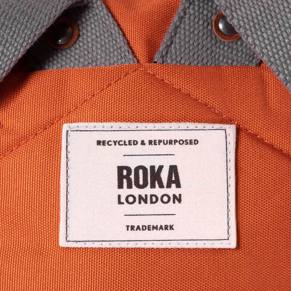 Roka London recycled and repurposed canvas backpack in atomic orange with grey accents and a white label.