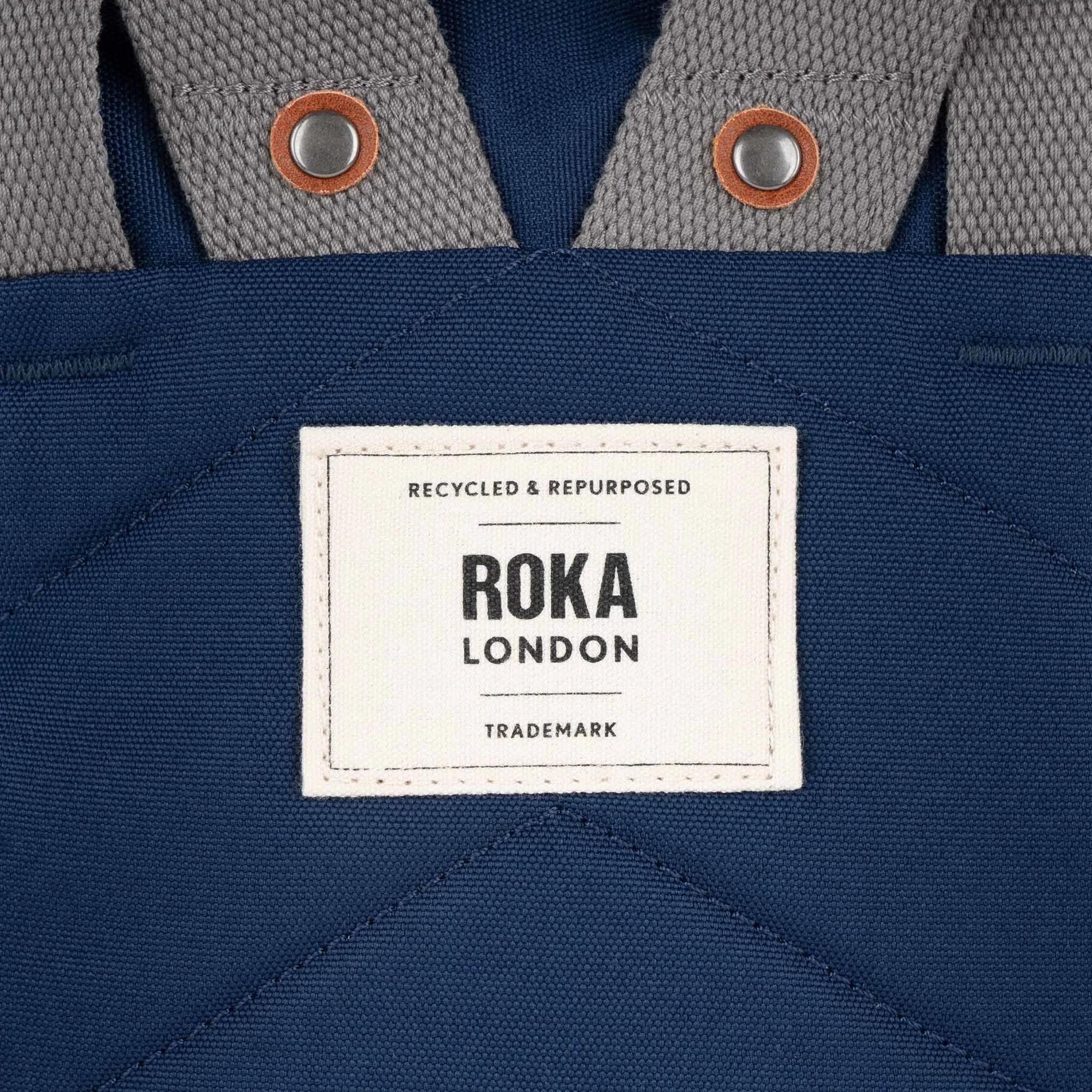 Close-up of Roka Finchley bag made from crisp blue recycled canvas with metal snap buttons and a white label.
