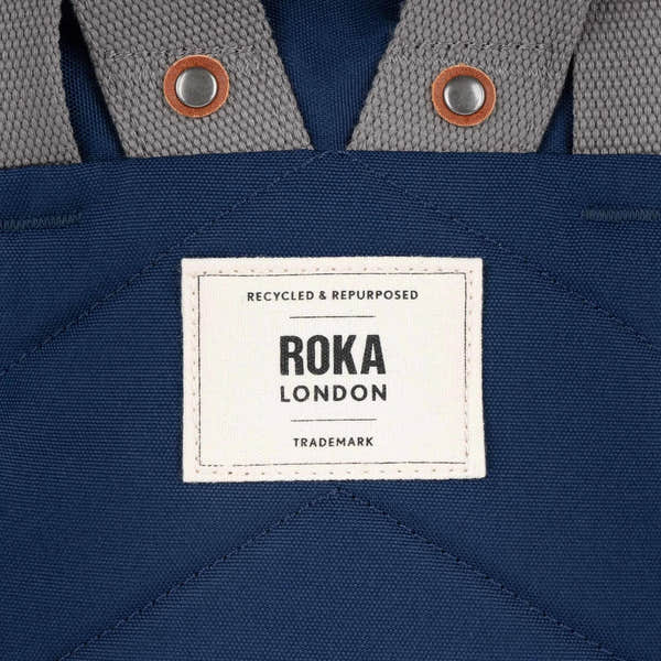 Close-up of Roka Finchley bag made from crisp blue recycled canvas with metal snap buttons and a white label.