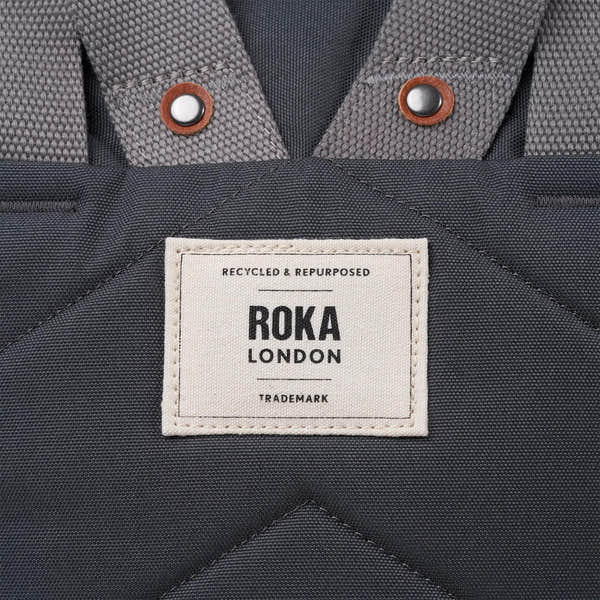 Roka Finchley A Faded Black Recycled Canvas backpack with grey straps and metal snap buttons.