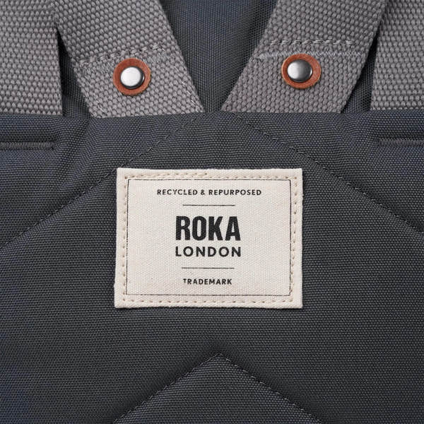 Roka Finchley A Faded Black Recycled Canvas backpack with grey straps and metal snap buttons.