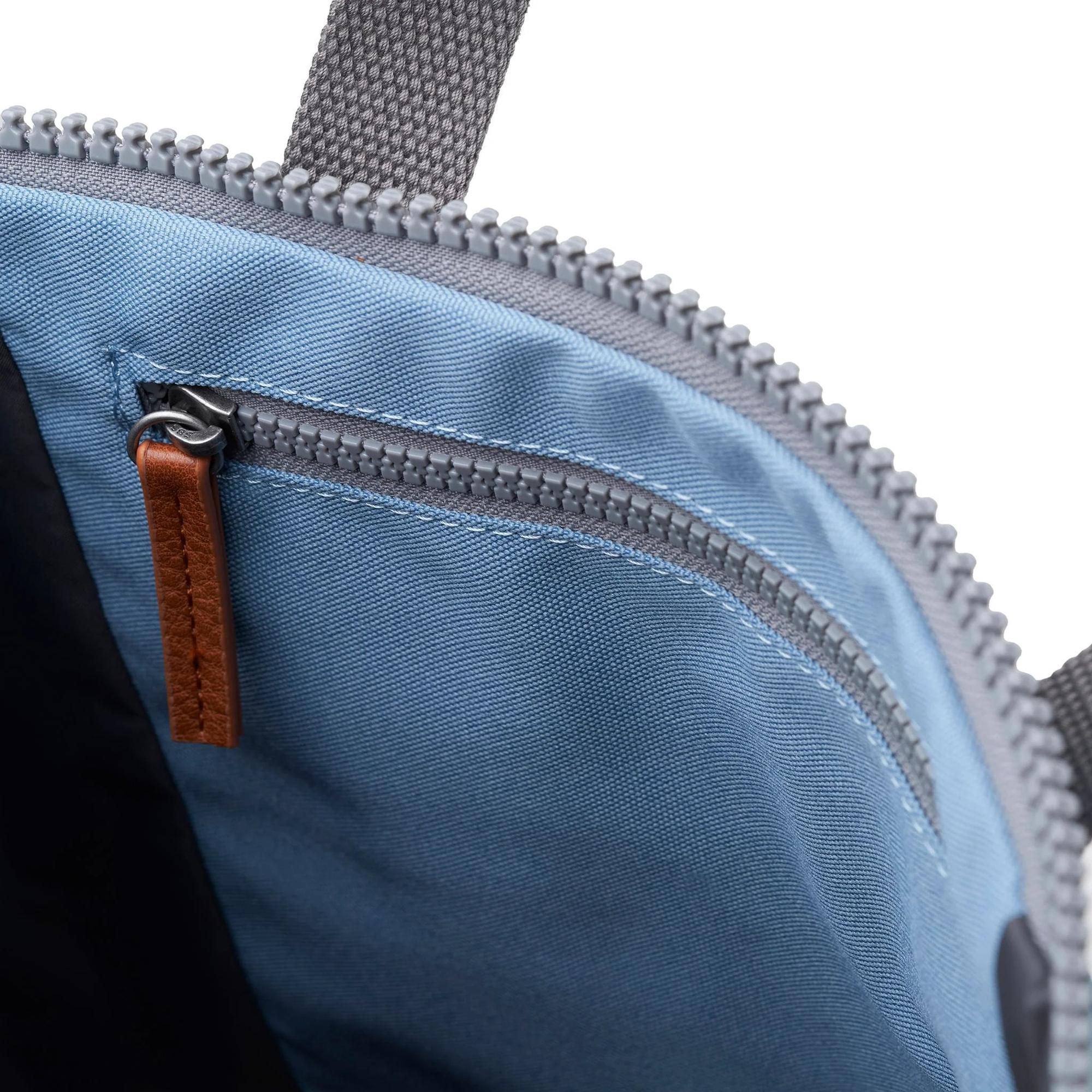 Close-up of Roka Finchley A Retro Blue Recycled Canvas backpack interior with front zipper pocket and brown leather pull tab.