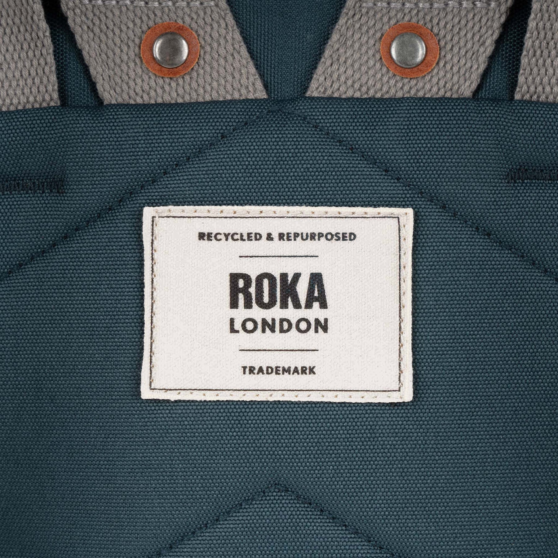 Roka Finchley A Smoke recycled canvas tote bag, close-up of label and textured fabric, grey and teal color, durable style.