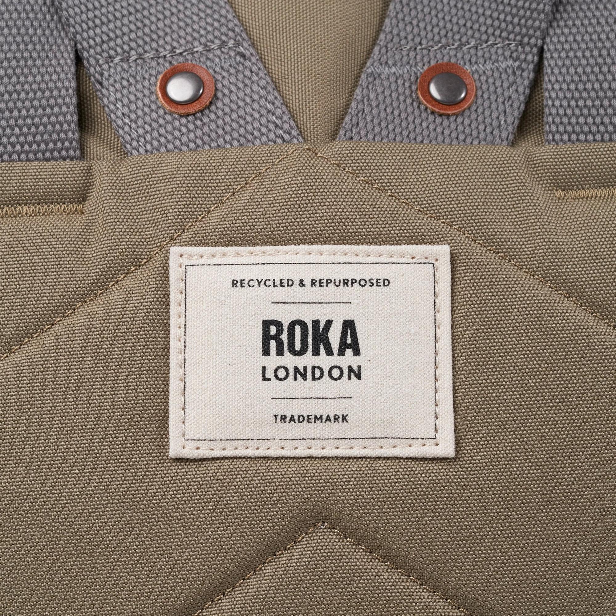 Roka Finchley taupe recycled canvas bag with fabric logo patch and dual metal snap buttons.