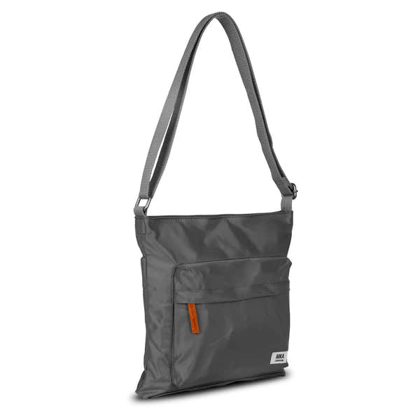 Roka Kennington B Crossbody Bag in recycled nylon, Graphite color, with front pocket, adjustable strap, and orange logo tag.