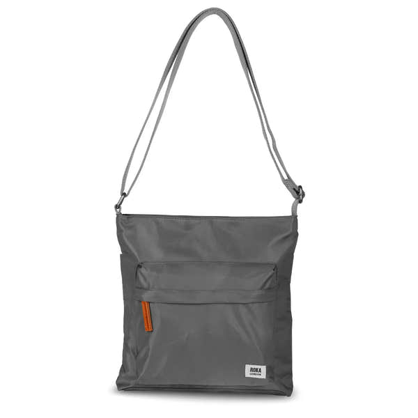 Roka Kennington B Crossbody Bag in recycled nylon with adjustable strap, graphite color, front zipper pocket, and logo detail.