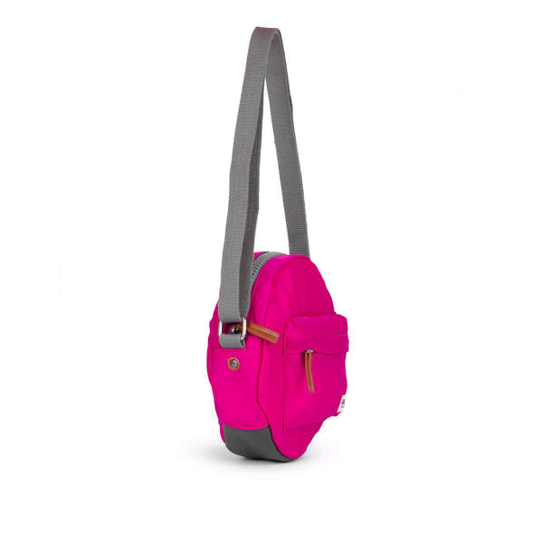 Roka Paddington B Candy small recycled nylon crossbody bag in vibrant pink with gray adjustable strap and brown zipper details.