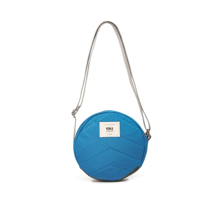 Roka Paddington B Seaport small recycled nylon crossbody bag in blue with adjustable strap and front label.