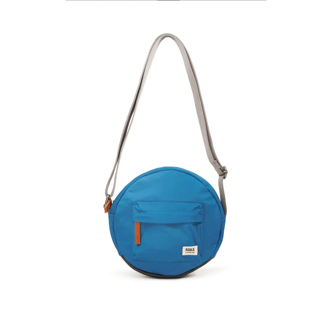 Roka Paddington B Seaport small recycled nylon crossbody bag in bright blue with front zip pocket and adjustable strap.