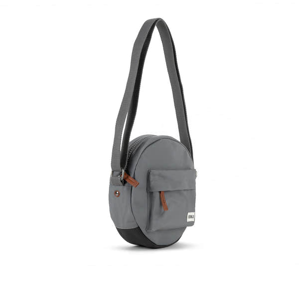 Roka Paddington B Stormy Small recycled nylon crossbody bag with front pocket, adjustable strap, and brown zipper detail.