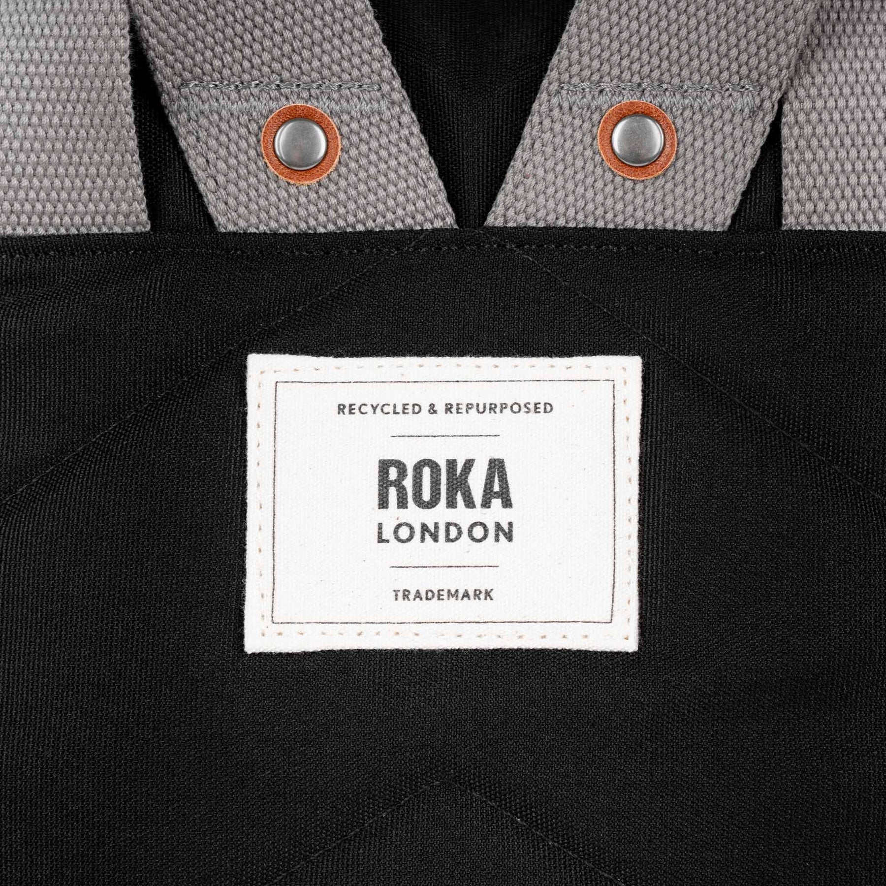 Roka Waterhouse recycled canvas ash zippered tote bag with grey and black fabric, metal snap accents, and a white branded label.