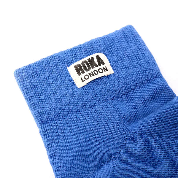 Roka Wembley Cotton Socks in Malibu Blue, showing close-up of fabric and label with "Roka London" branding.