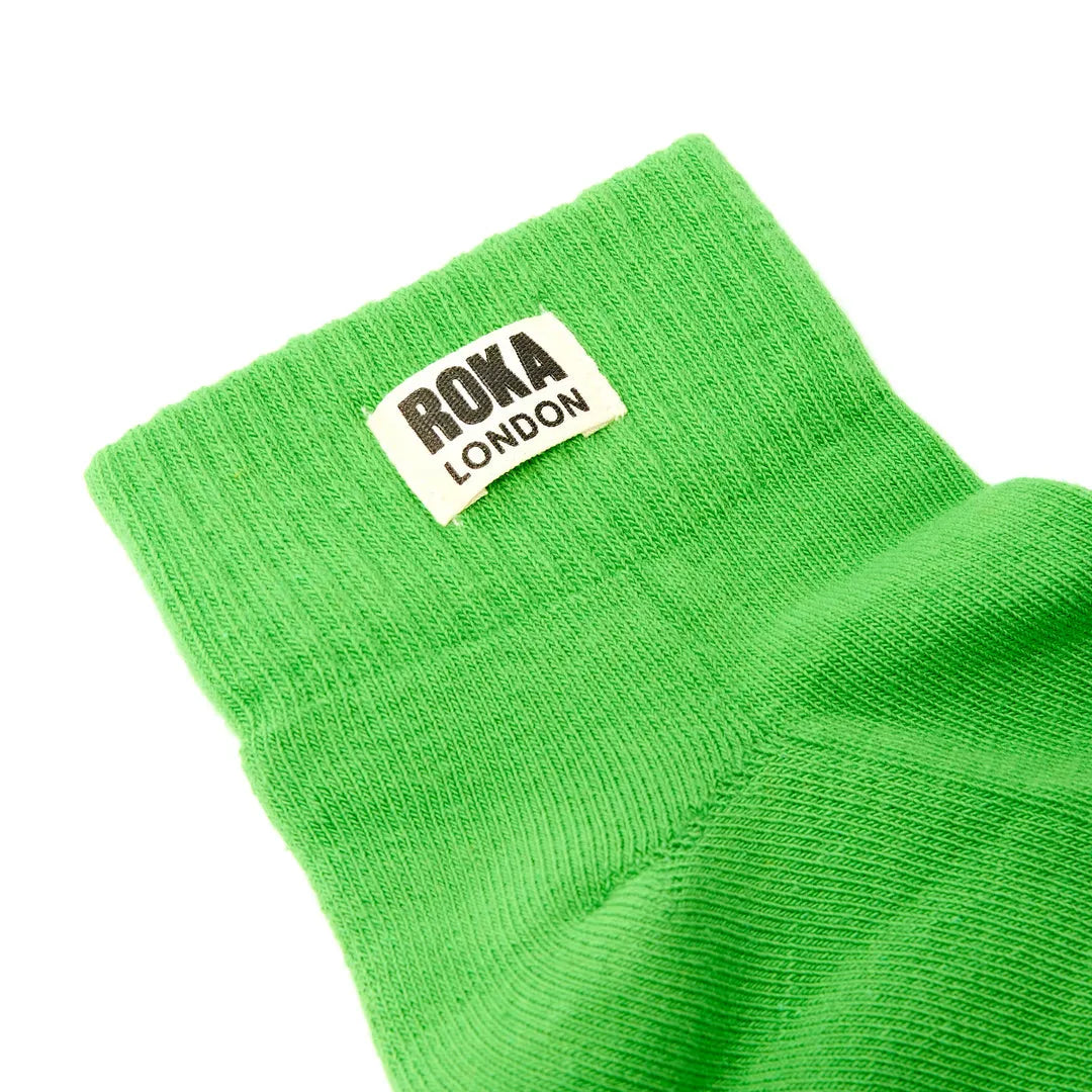 Green Roka London cotton sock with black and white logo tag, soft knit fabric, vibrant lime color, and ankle-length design.