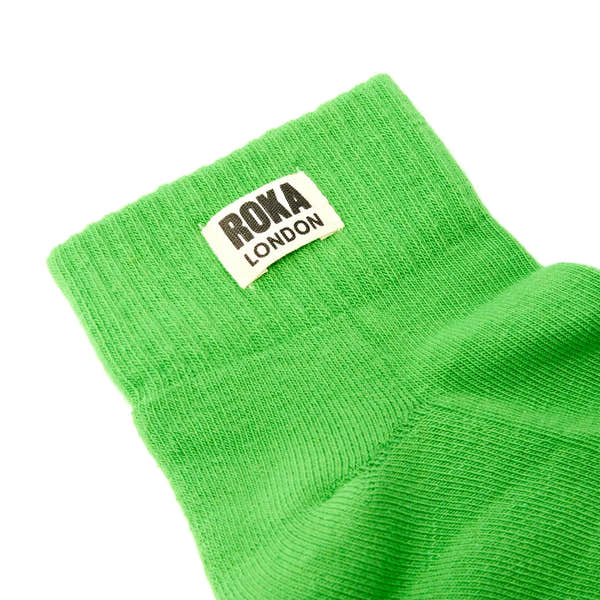Green Roka London cotton sock with black and white logo tag, soft knit fabric, vibrant lime color, and ankle-length design.