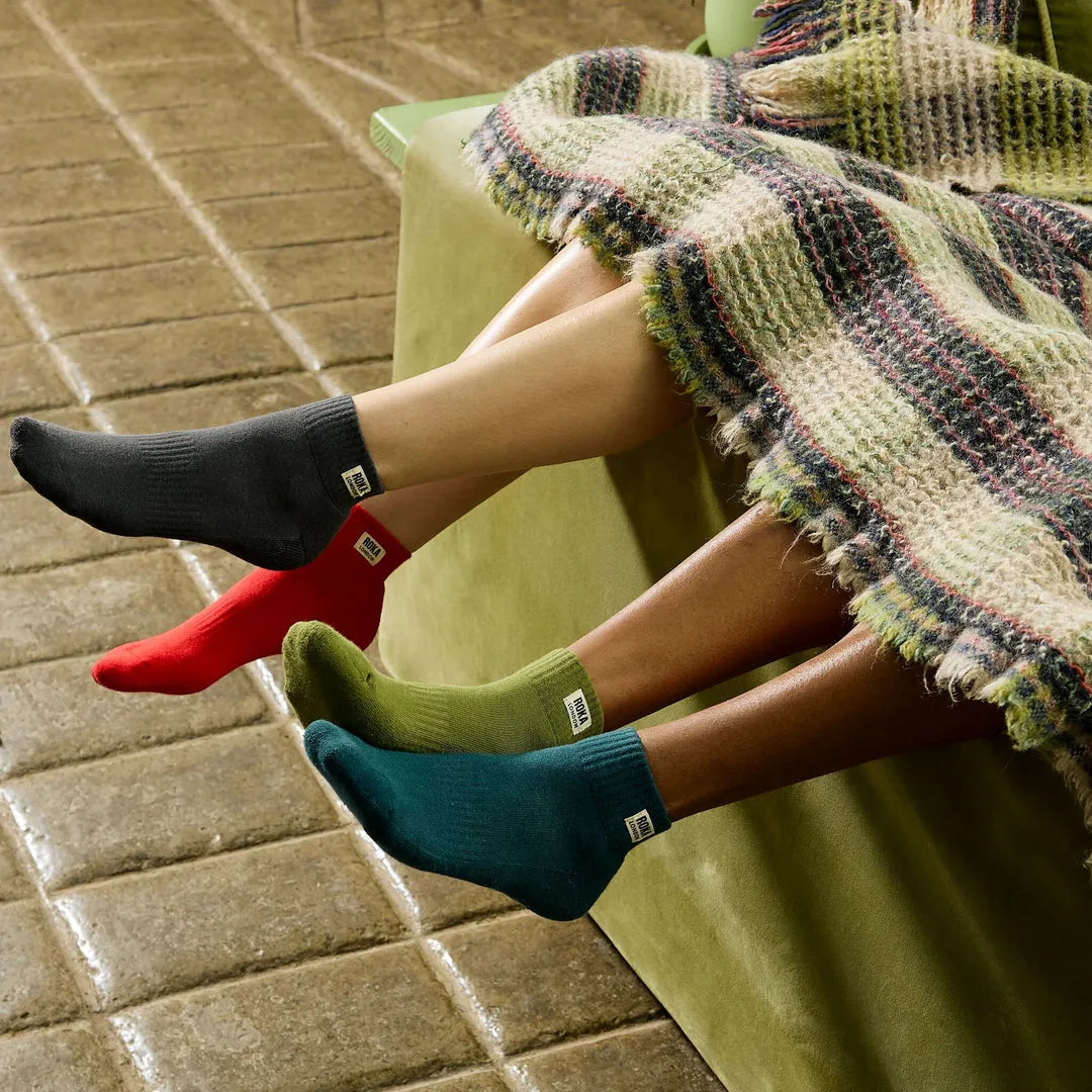 Roka Wembley Ladies Cotton Socks in cranberry, black, green, and teal, shown on legs under a blanket, cozy indoor setting.