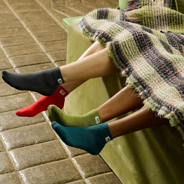 Roka Wembley Ladies Cotton Socks in cranberry, black, green, and teal, shown on legs under a blanket, cozy indoor setting.