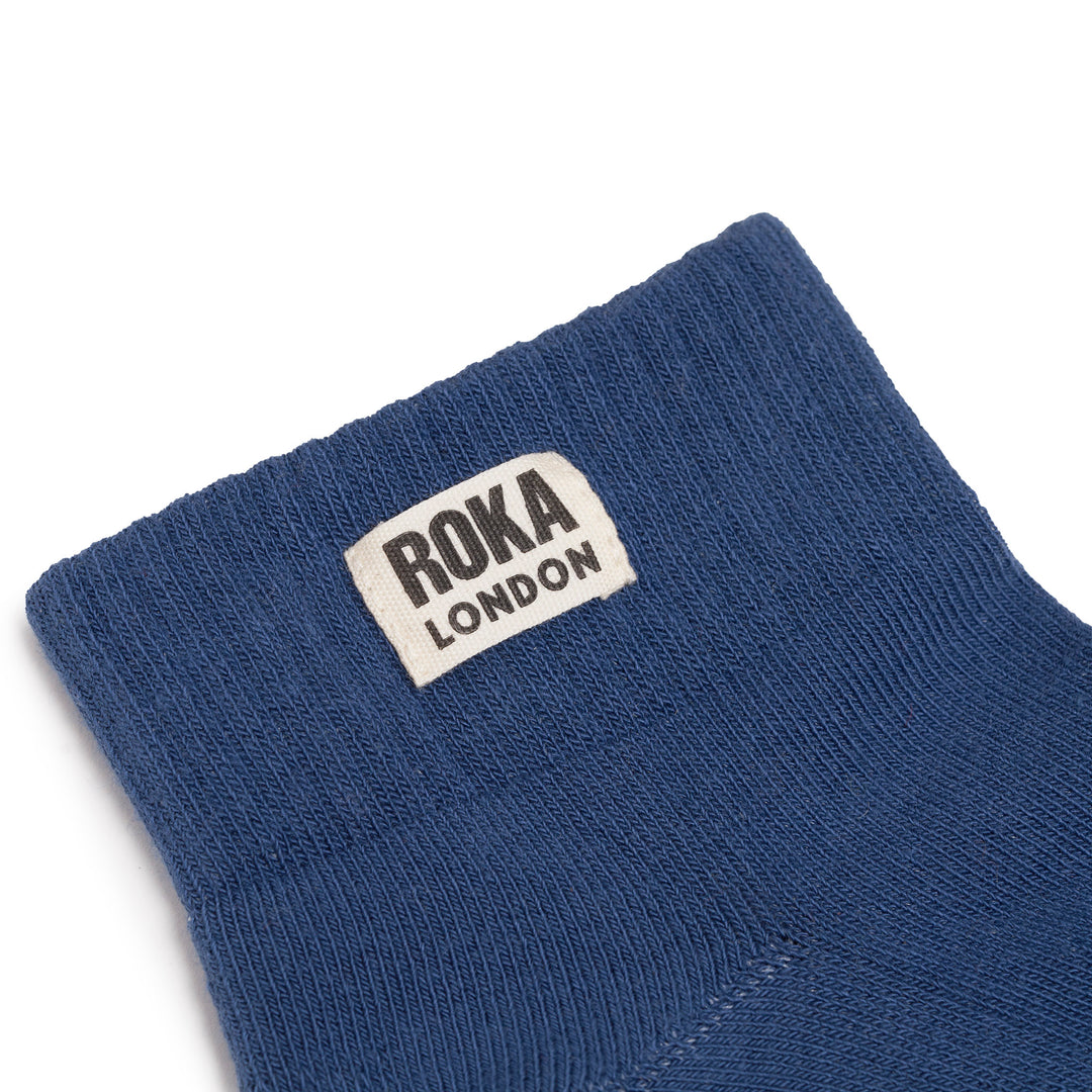 Roka Wembley Womens Coastal Blue Organic Cotton One Size sock with Roka London label, close-up of knitted fabric and stitched edge.