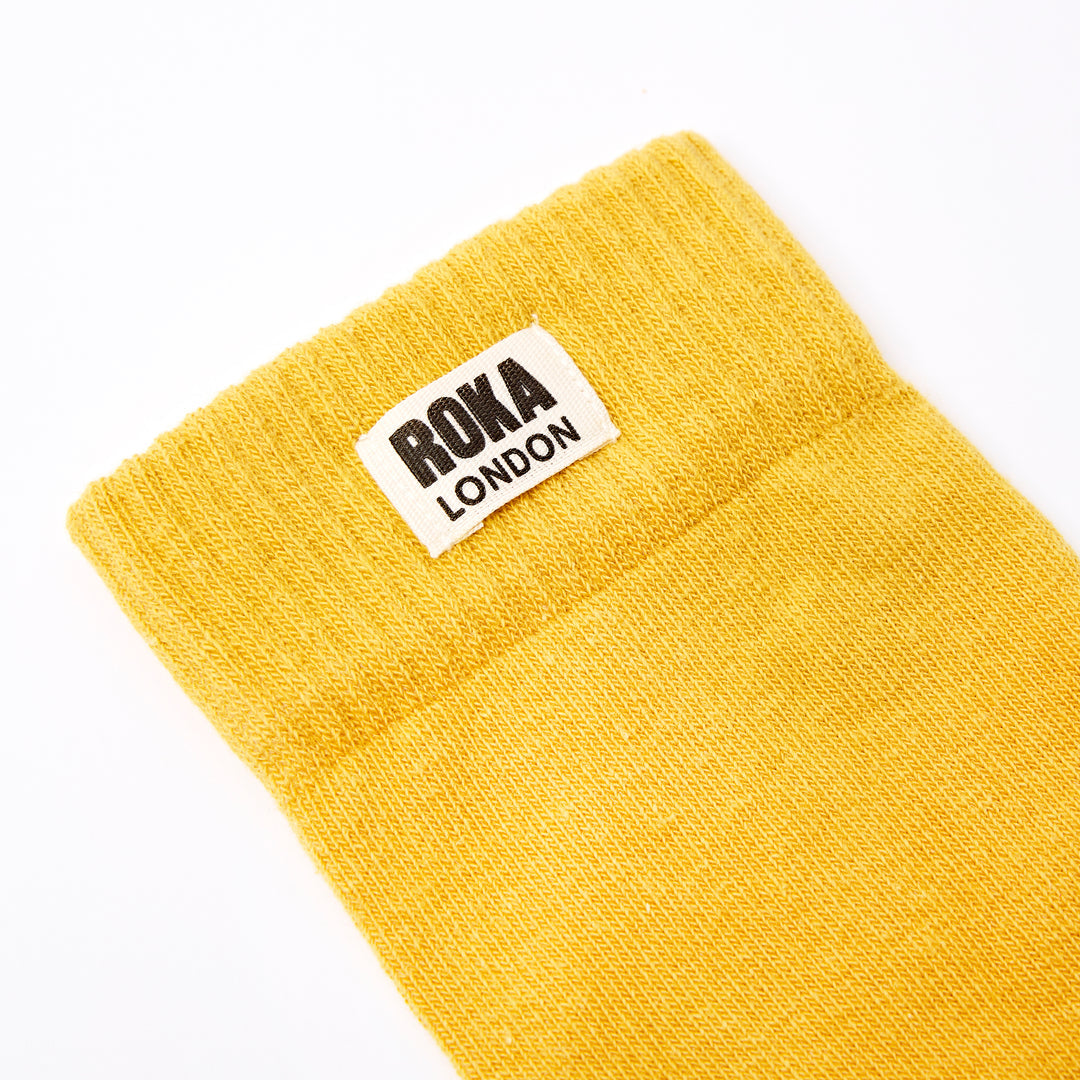 Yellow cotton crew sock with ROKA London logo label, one size, casual athletic style.