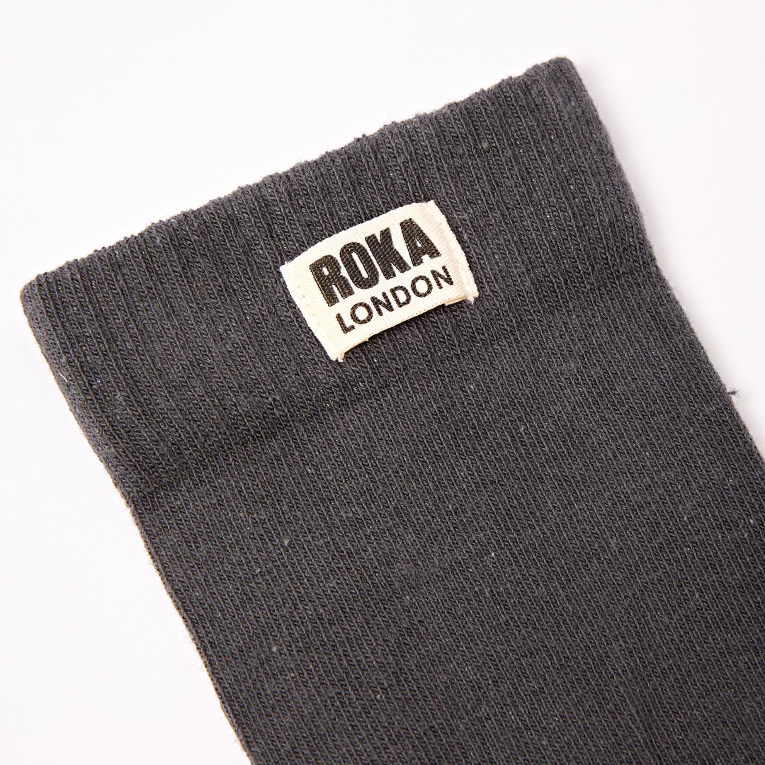 Roka London men's cotton crew sock in faded black, size one, with logo tag, close-up view.
