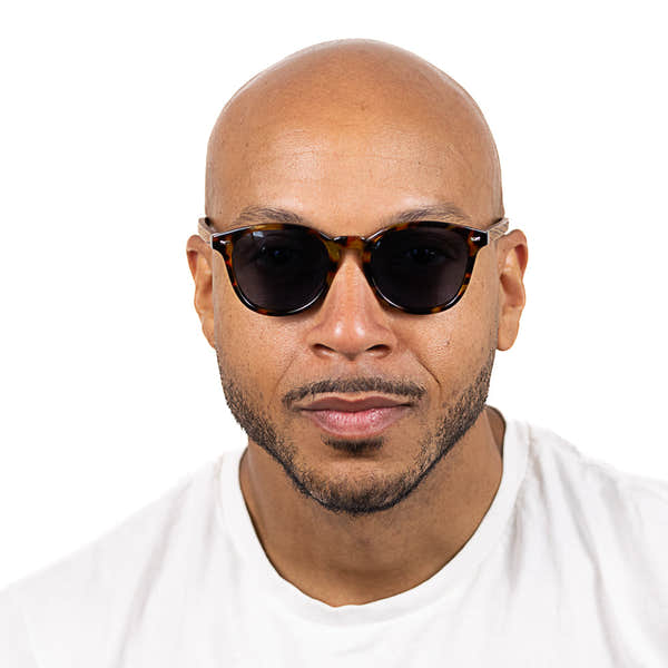 Man wearing SOEK Taine Tortoise Shell sunglasses with blue lenses and walnut arms, close-up portrait, white background.